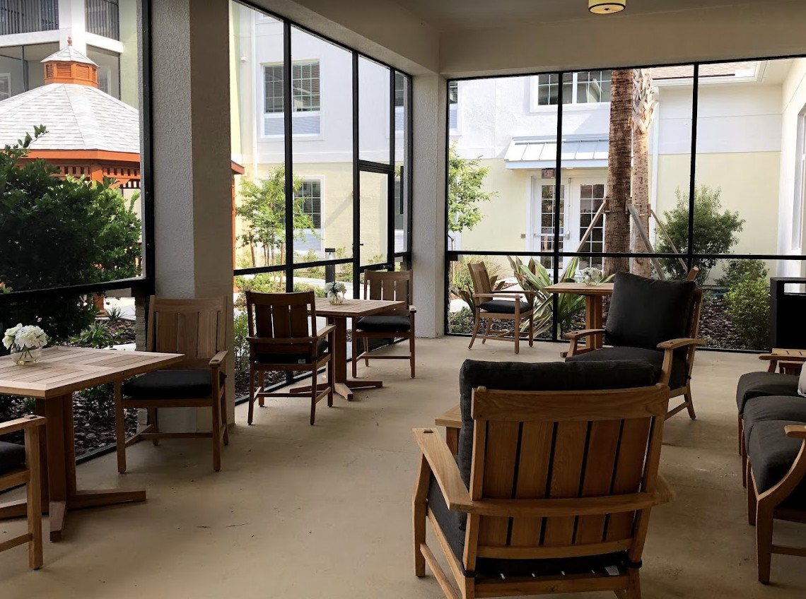 A cozy indoor seating area with tables and chairs, surrounded by large windows letting in natural light.