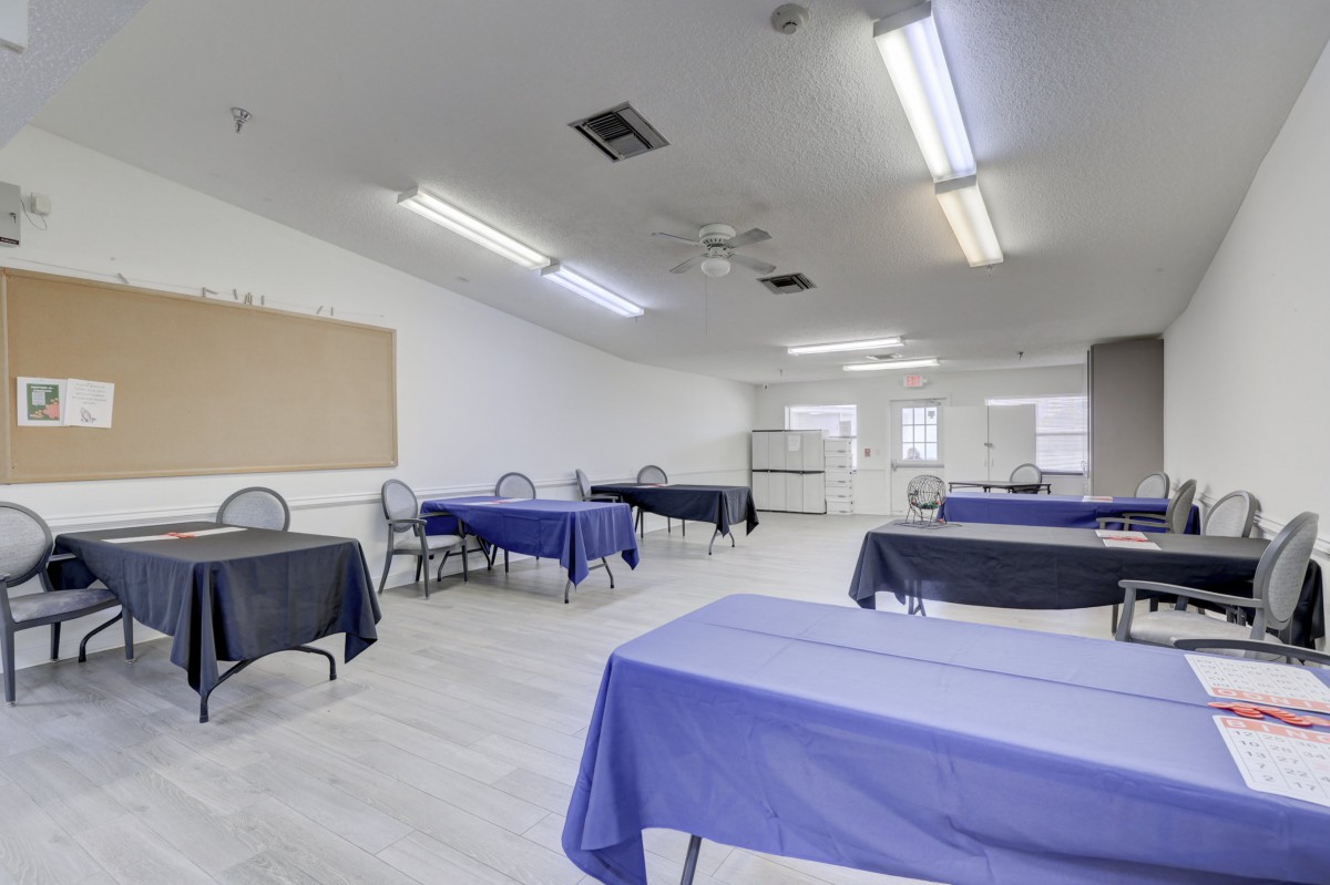 An empty classroom with tables covered in blue tablecloths and chairs arranged around them.