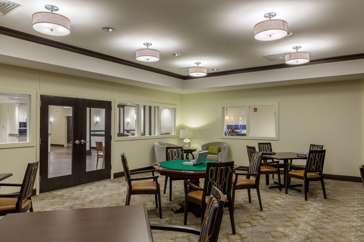 A well-lit interior room with multiple tables and chairs, featuring modern lighting and carpeted floors.
