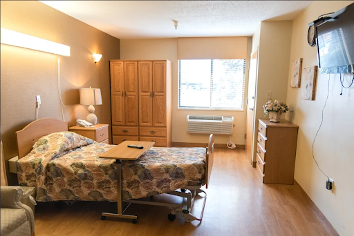 A spacious and well-lit hospital patient room with essential furniture and a view outside.