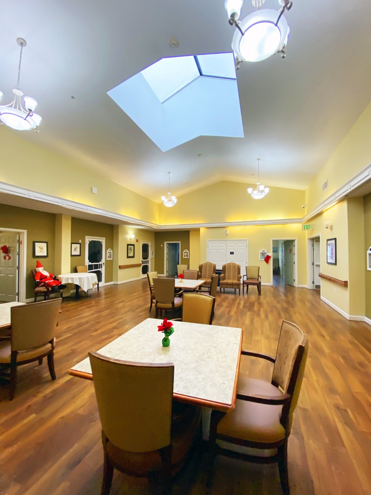 A spacious and well-lit communal area with tables and chairs, featuring a skylight and hardwood flooring.