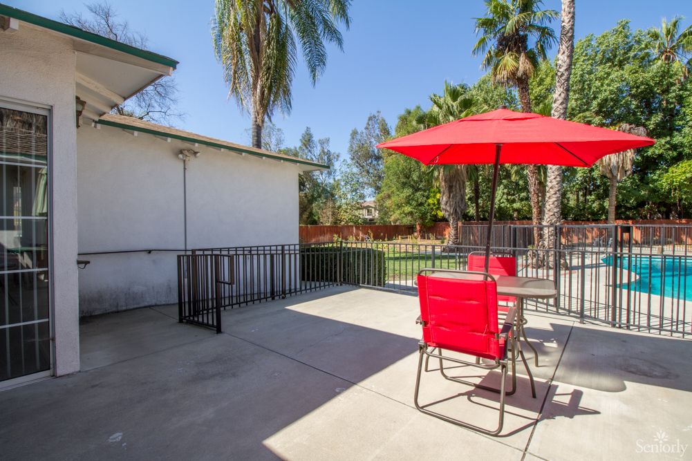 A sunny patio with red chairs and an umbrella, surrounded by palm trees.