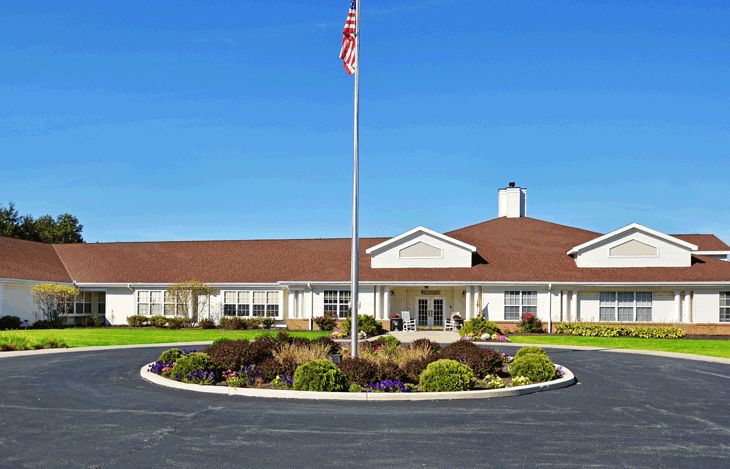 A one-story building with an American flag in front, surrounded by a landscaped circular driveway.