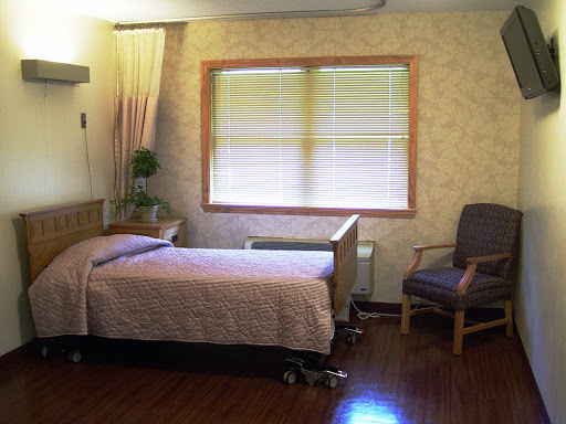 A serene hospital room featuring a bed, an armchair, and natural light from the window.