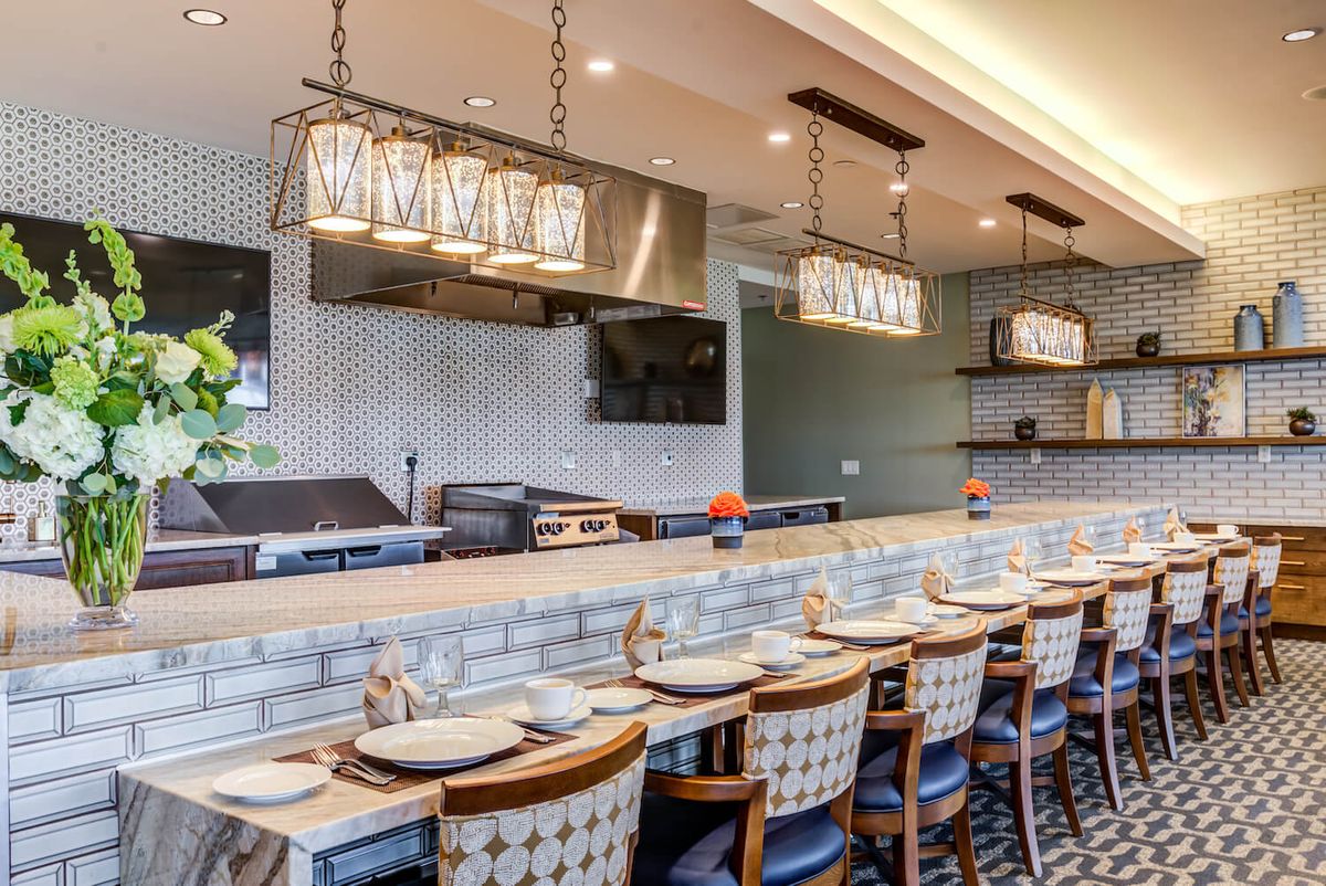 A modern restaurant interior featuring a bar seating area with stylish light fixtures and neatly arranged dinnerware.