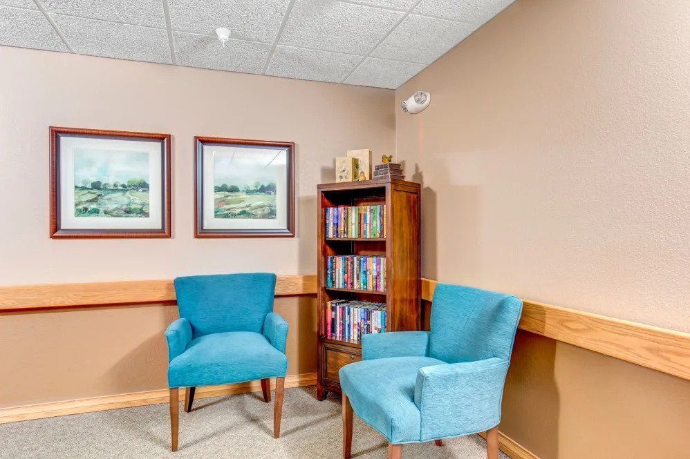 Cozy waiting area with two blue chairs and a bookshelf.