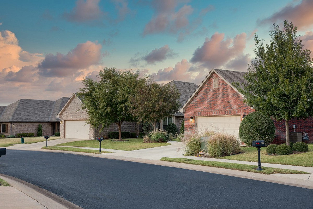 A quiet suburban street lined with houses and trees under a partly cloudy sky.