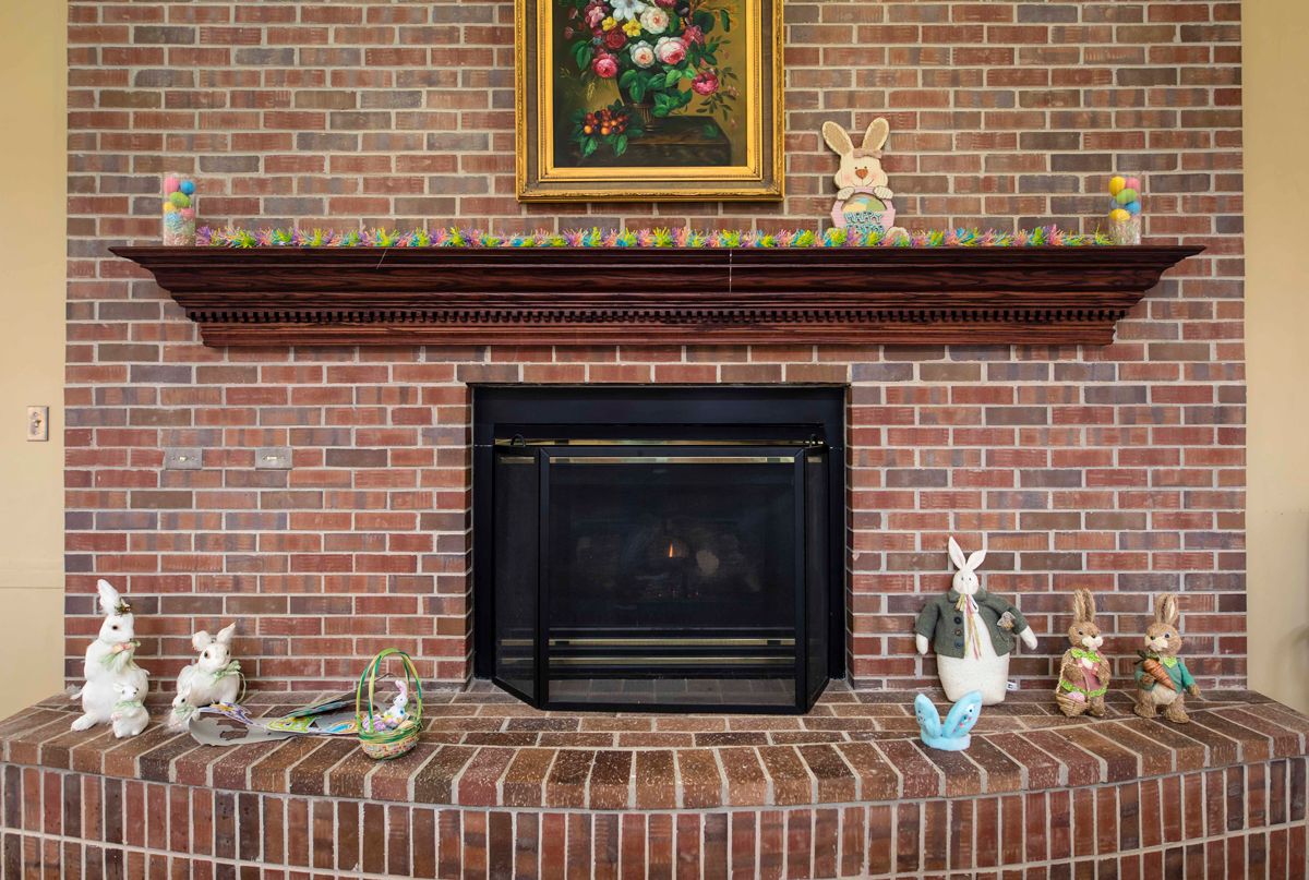A cozy brick fireplace adorned with a floral painting and bunny figurine decorations.