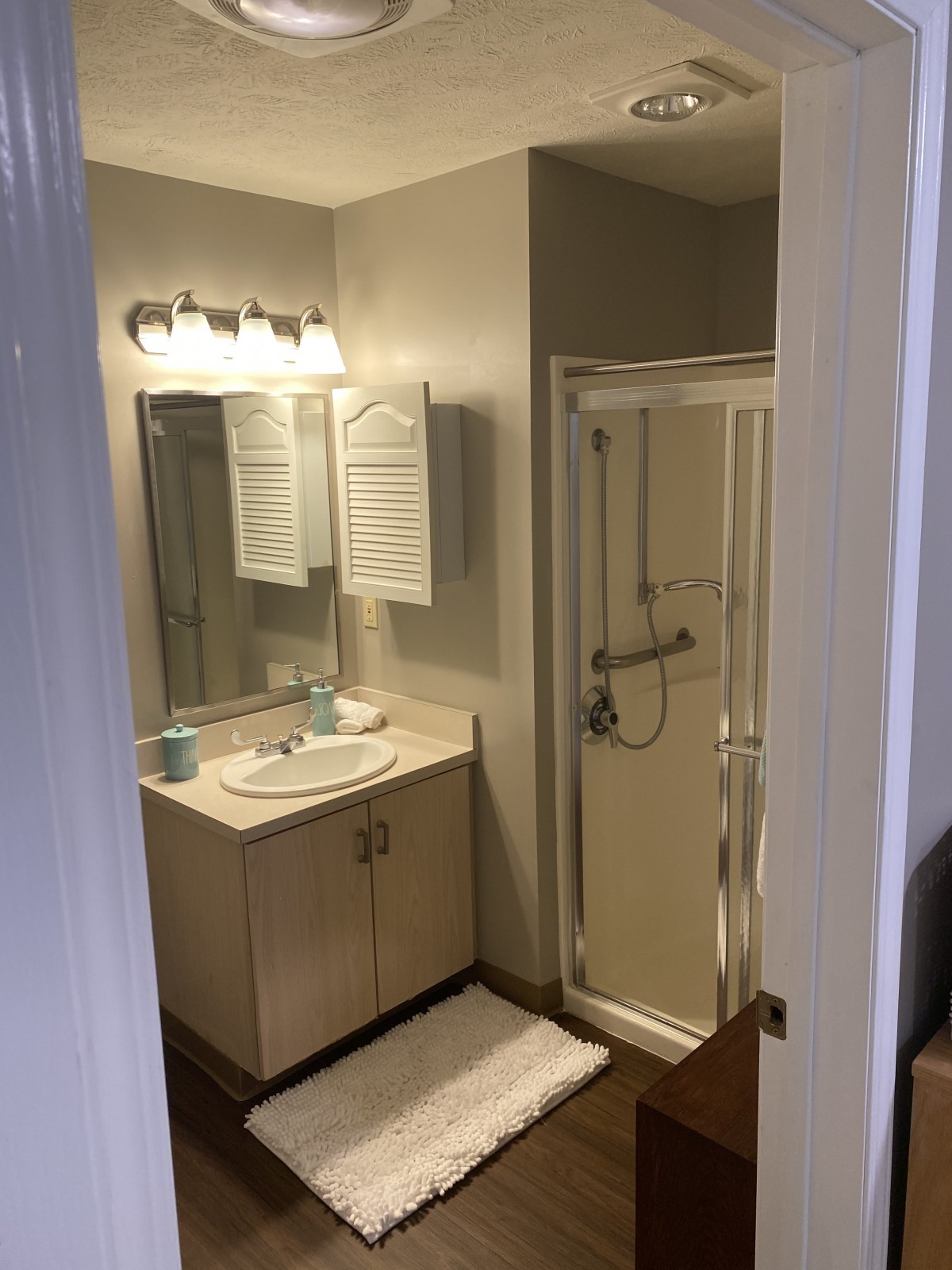A well-lit bathroom with a vanity sink, mirror, and shower enclosure.