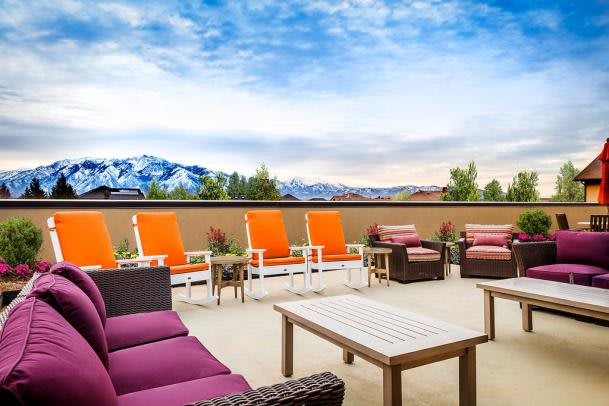 A vibrant patio with colorful seating offers a scenic view of mountains under a blue sky.