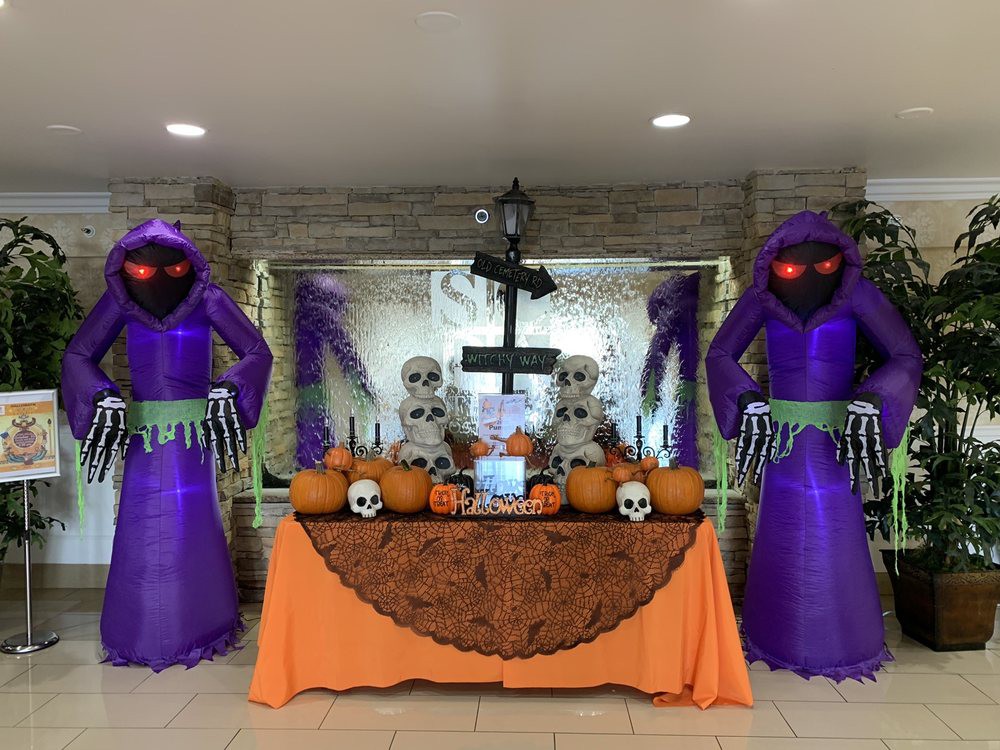 A festive Halloween display featuring two inflatable purple reapers, pumpkins, and skeletons on a decorated table.