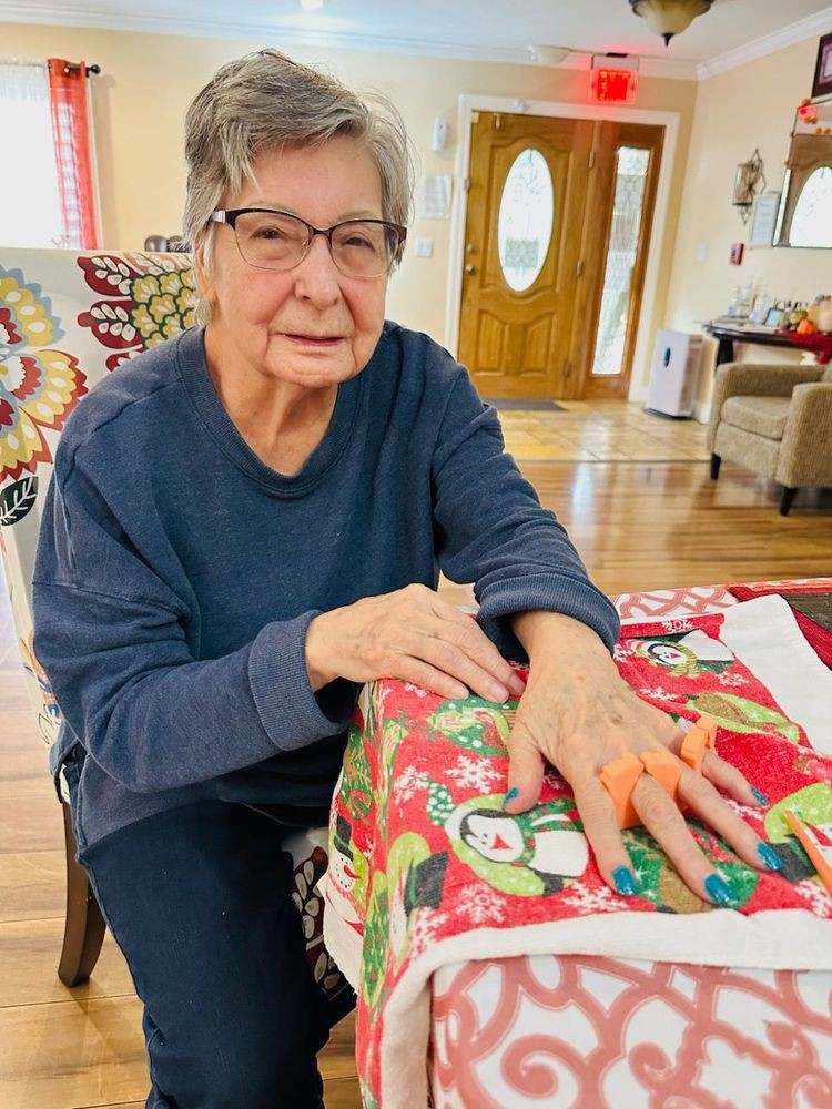 An elderly woman seated indoors with a colorful blanket over her lap.