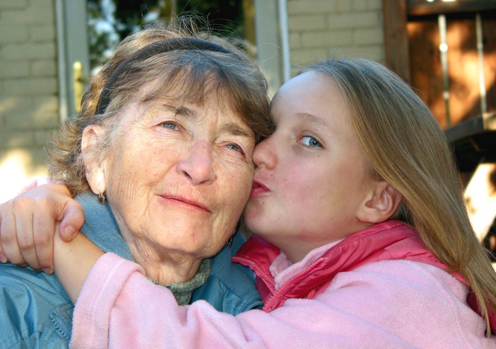 A young girl affectionately kisses her grandmother outdoors.