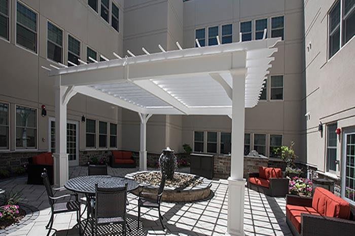 A courtyard with a white pergola providing shade over outdoor seating and patio furniture.