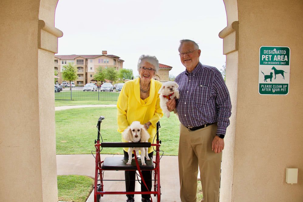 An elderly couple smiling with their two small dogs outdoors.
