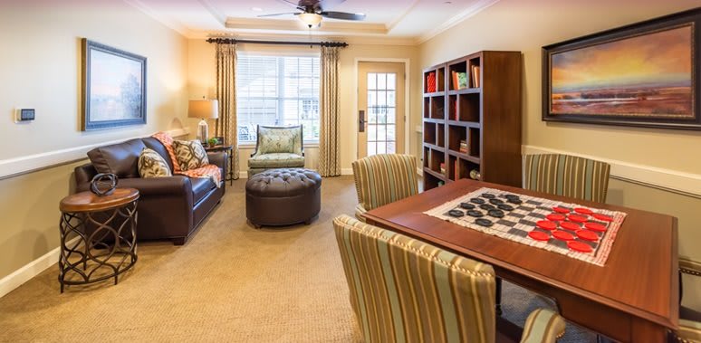 A cozy living room featuring comfortable seating, a large window with curtains, and a bookshelf filled with books.