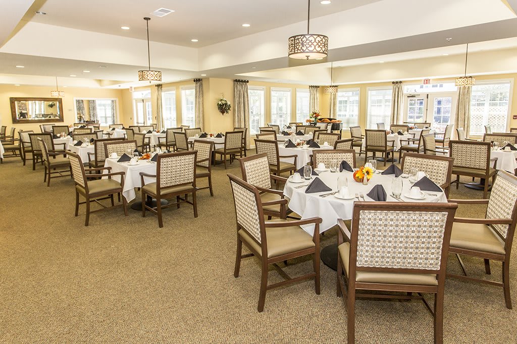A well-decorated dining room with multiple tables set elegantly with white tablecloths and chairs.