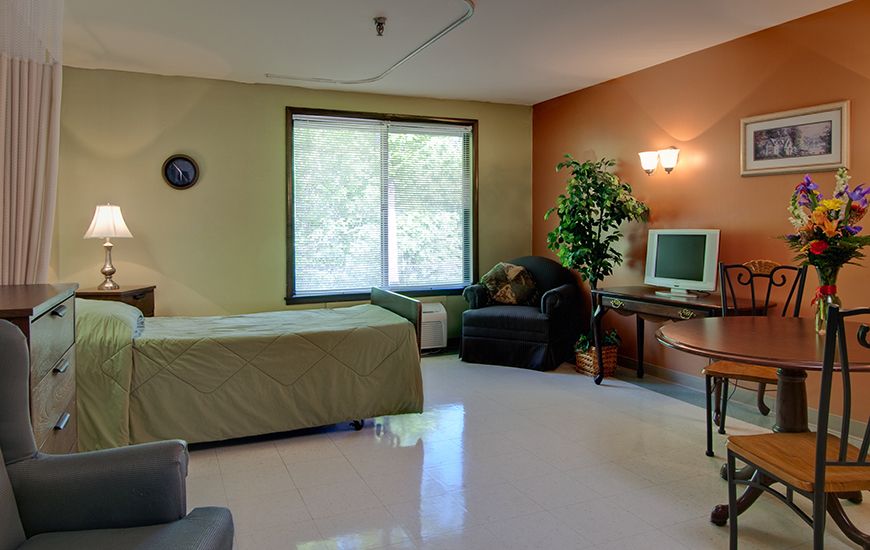 A cozy bedroom featuring a bed, desk with a computer, chair, and large window.
