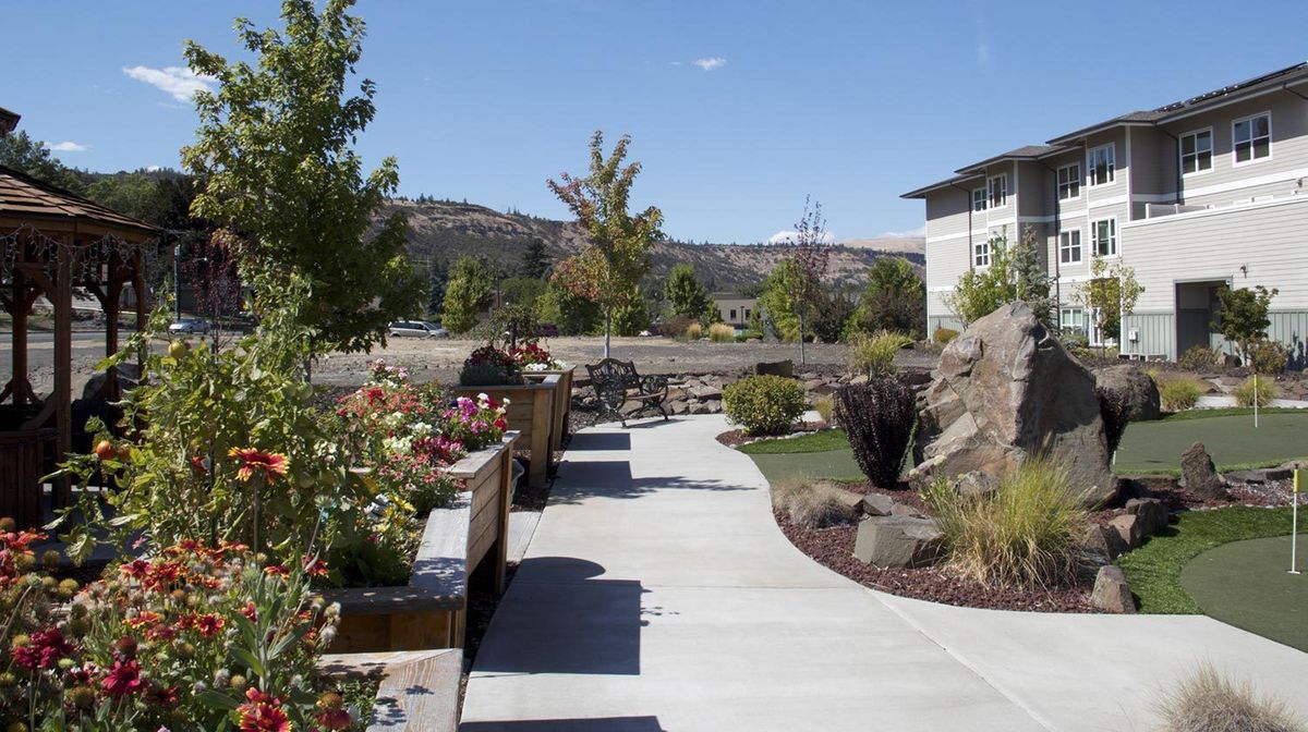 A scenic garden pathway with benches and trees under a clear blue sky.