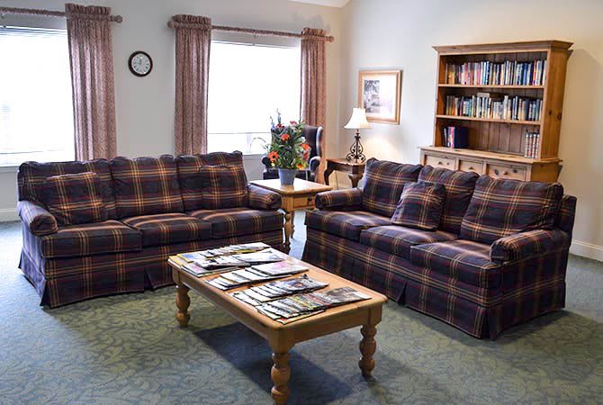 A cozy living room with plaid sofas, a wooden coffee table, and a bookshelf filled with books.