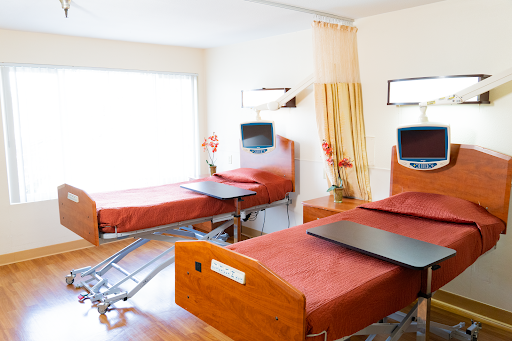 A modern patient room featuring two hospital beds with red bedding and equipped with televisions.
