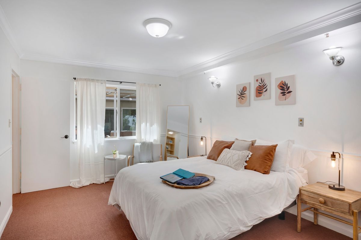 A cozy and bright bedroom with a neatly made bed, decorative pillows, and wall art.