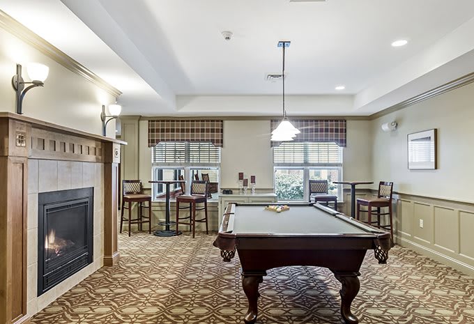 A cozy game room featuring a pool table, fireplace, and seating area with windows providing natural light.