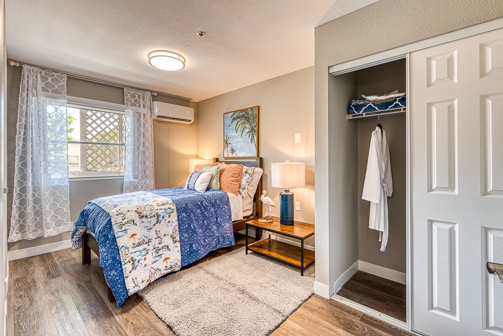 A cozy bedroom with a neatly made bed, featuring blue and white bedding, a small closet, and a bedside table with a lamp.