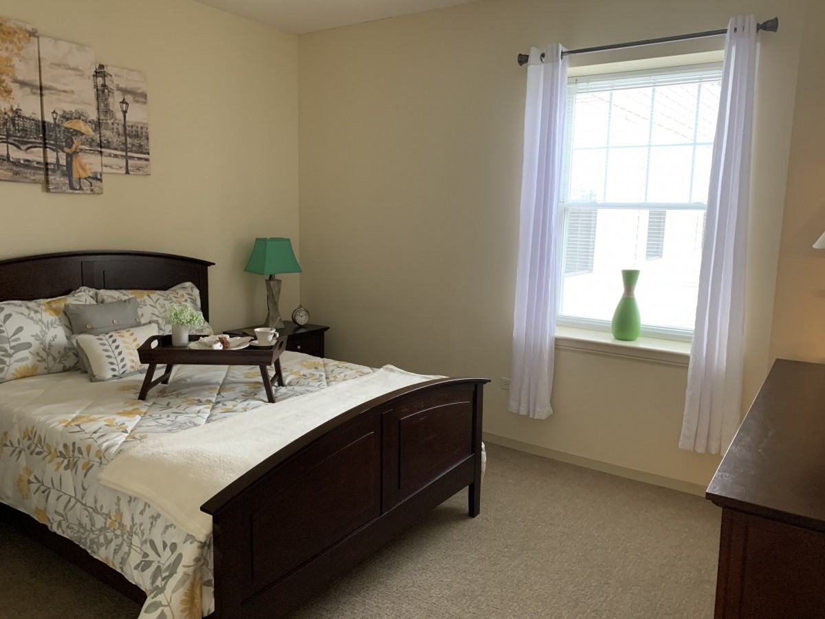 A cozy bedroom with a bed, bedside lamp, and window with curtains.