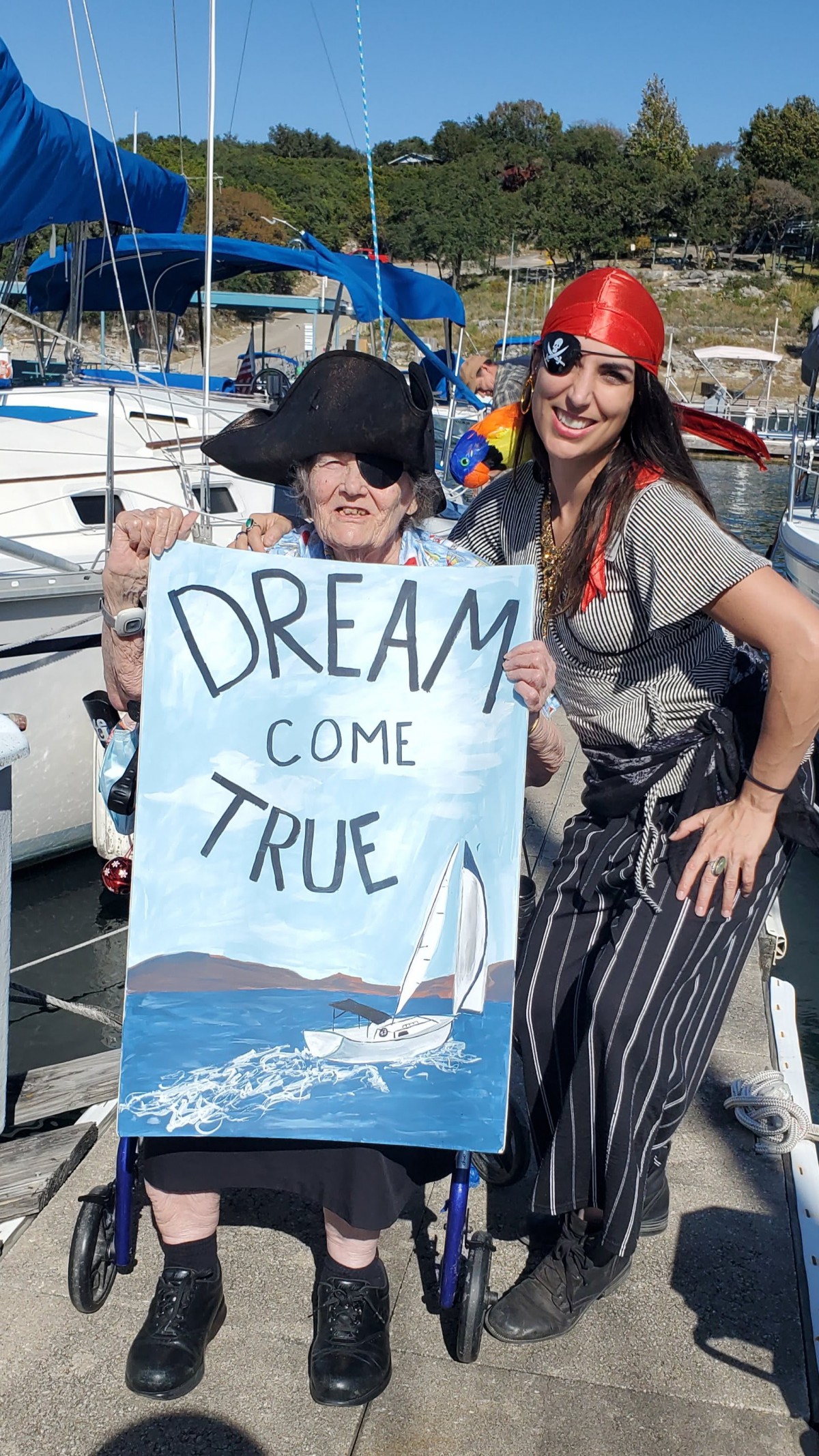 Two people dressed as pirates holding a 'Dream Come True' sign by the marina.