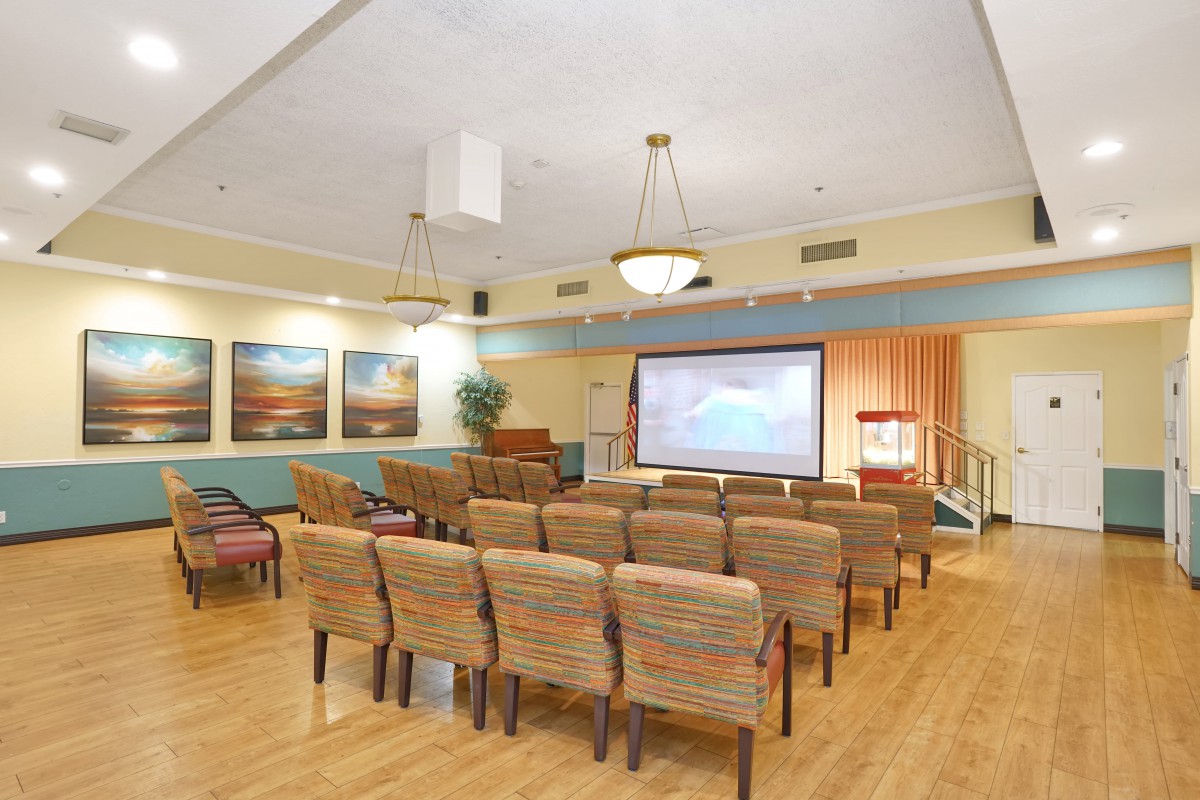 A well-lit conference room with rows of chairs facing a large projector screen, suitable for meetings or presentations.