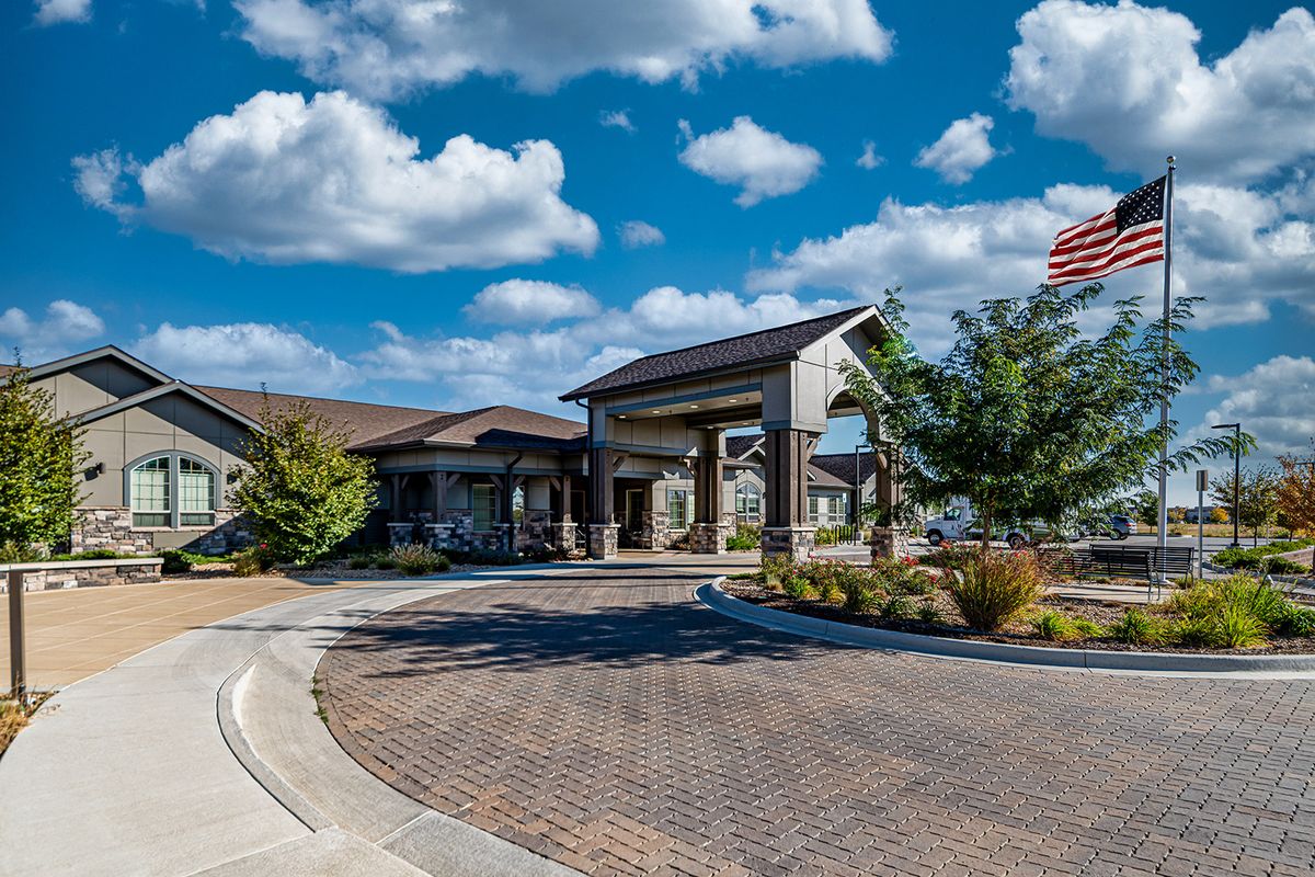 A modern building with a wide driveway under a blue sky with clouds.