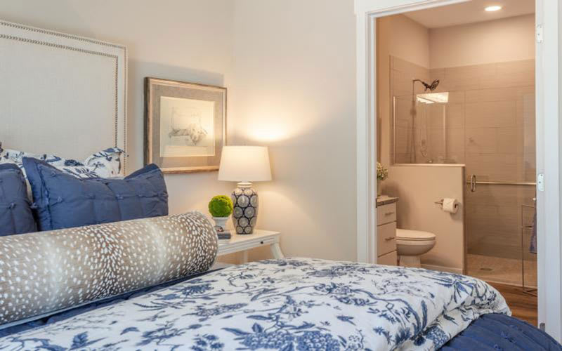 A cozy bedroom with soft lighting, featuring a bed with patterned bedding and an adjacent bathroom.