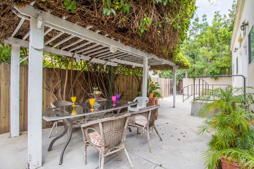 A cozy outdoor patio with a pergola and seating area, surrounded by lush greenery.