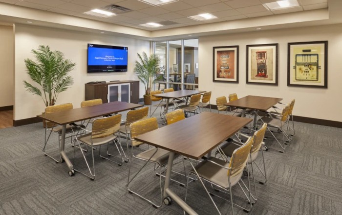 A modern conference room equipped with tables, chairs, a television, and indoor plants.