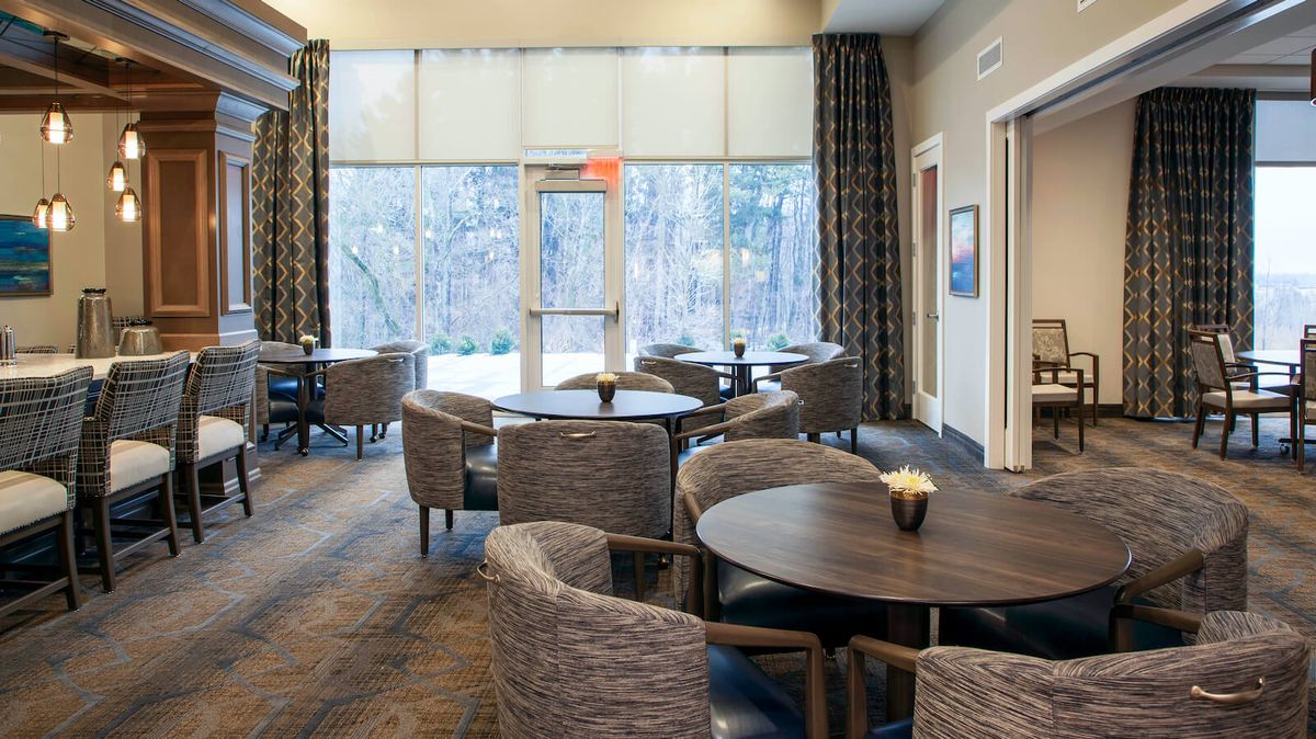 A modern dining area with round tables and stylish chairs, featuring large windows with a view.