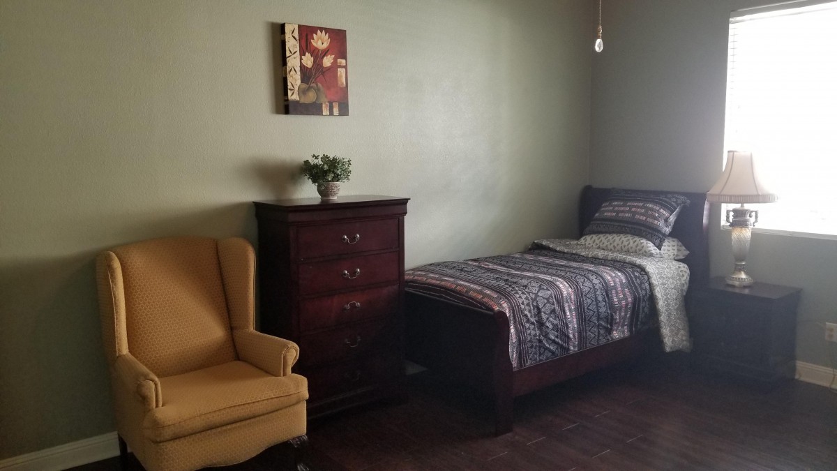 A simple bedroom with a single bed, wooden dresser, and armchair.