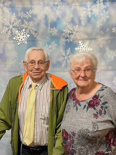 A cheerful elderly couple posing together in a festive setting with snowflake decorations.