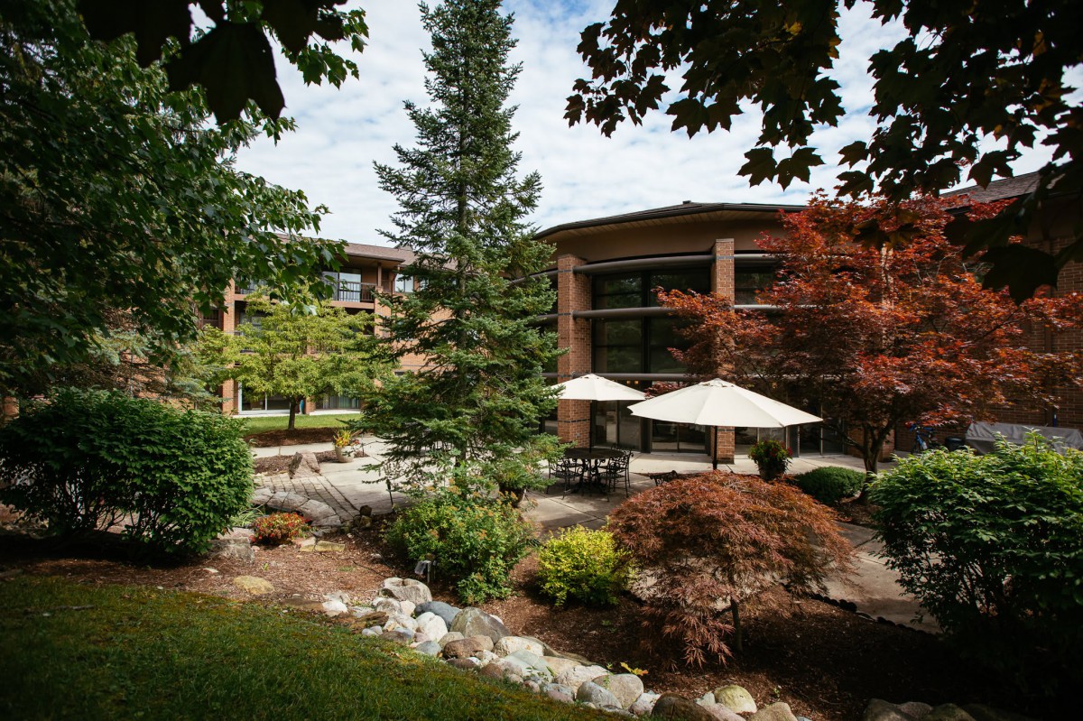A serene garden with a modern building in the background, surrounded by lush greenery and shaded by large umbrellas.