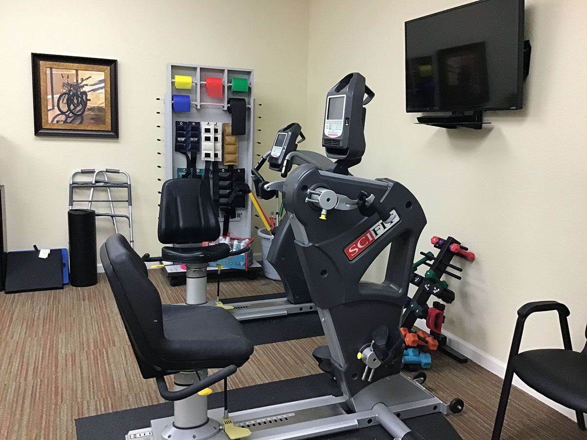 A gym room featuring a recumbent exercise bike, a rack of weights, and a television mounted on the wall.