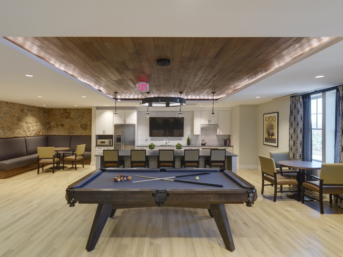 A modern entertainment room featuring a pool table and kitchen area.