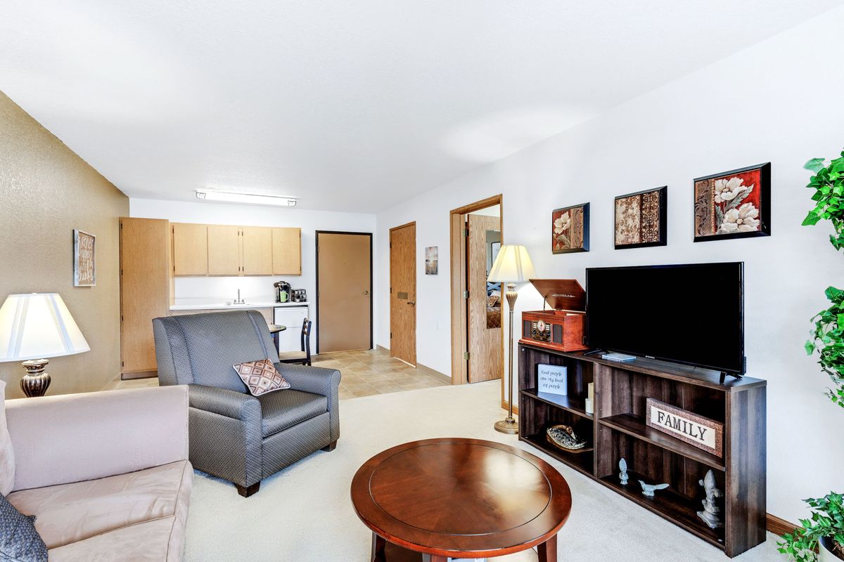 A cozy living room with comfortable seating, a television, and a view into the adjoining kitchen.