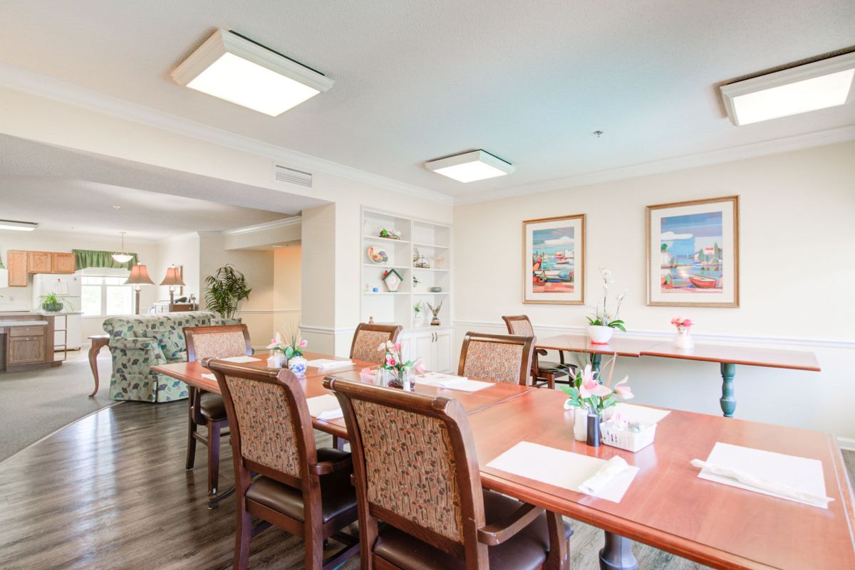 A bright and inviting dining room with a large wooden table surrounded by chairs, decorated with artwork on the walls.