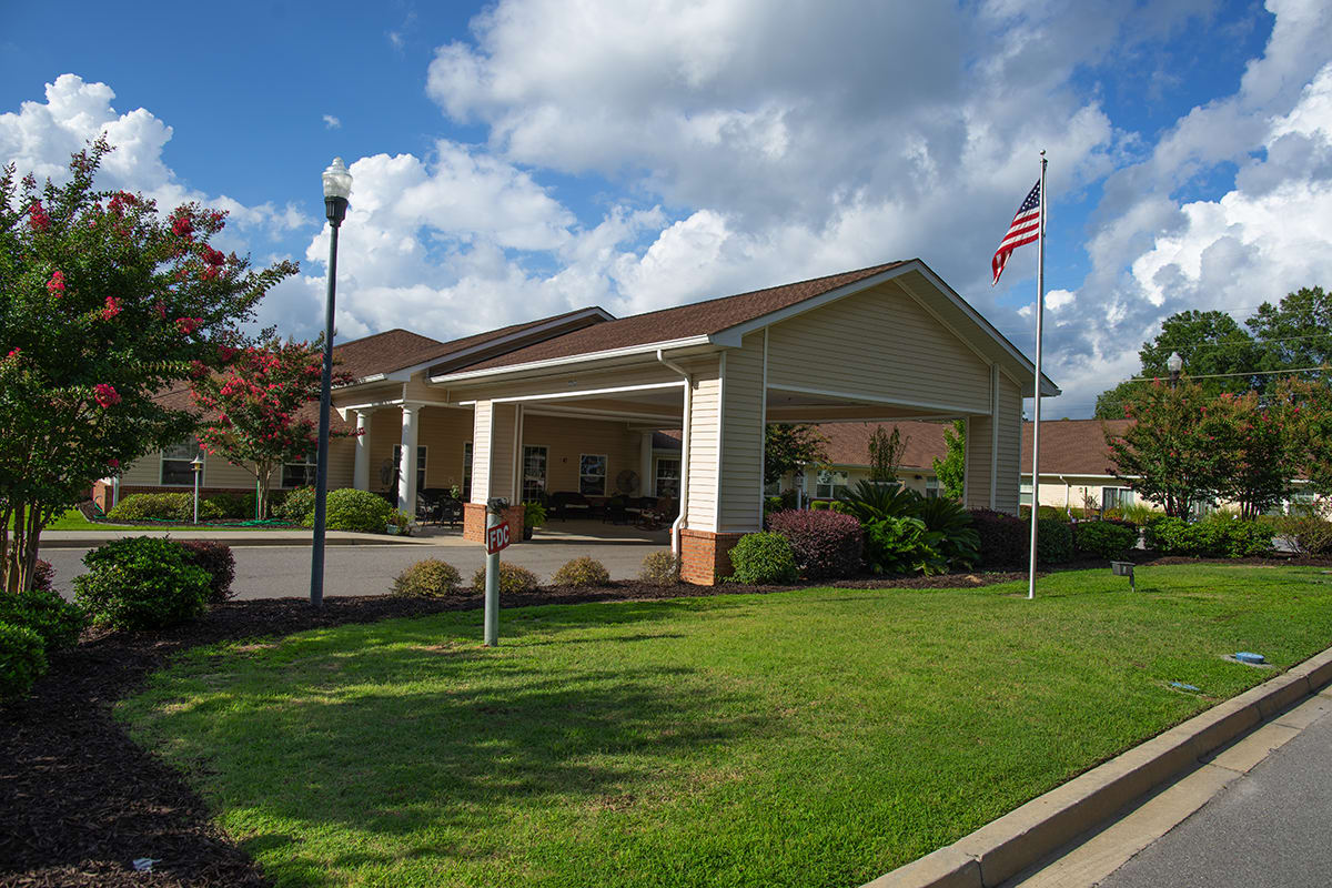 A building entrance with a covered driveway and an American flag flying, surrounded by well-maintained landscaping under a partly cloudy sky.