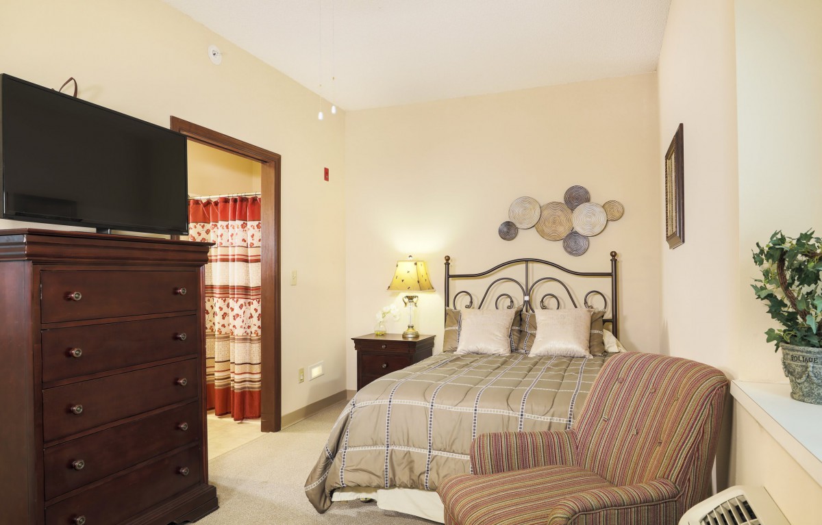 A cozy bedroom with a neatly made bed, decorative wall art, and a television atop a dresser.
