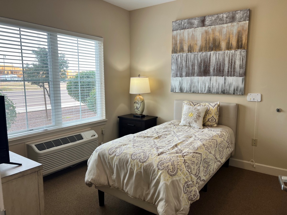 A cozy bedroom with a single bed, lamp, and abstract wall art.