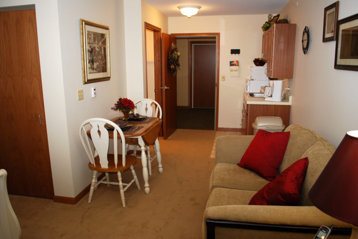 A cozy living room with a small dining area, featuring a sofa, dining table, and chairs in a warmly decorated interior.