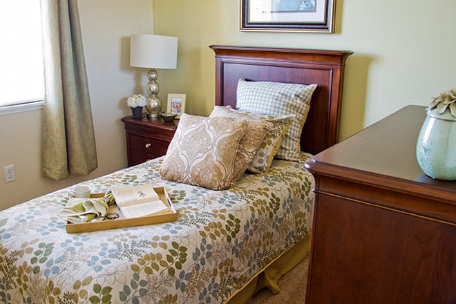 A cozy bedroom featuring a neatly made single bed with decorative pillows, accompanied by a nightstand and lamp.