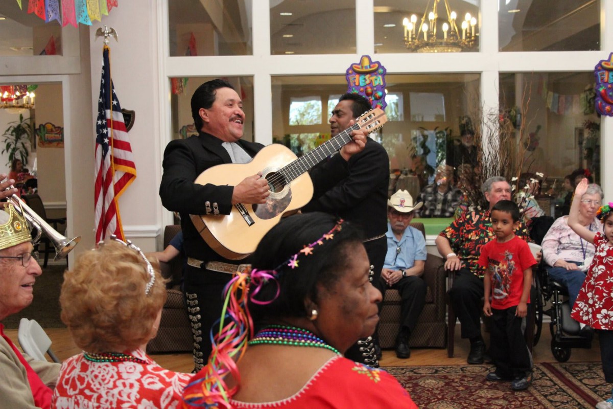 Musicians performing with a guitar at an indoor cultural celebration, surrounded by an attentive audience.