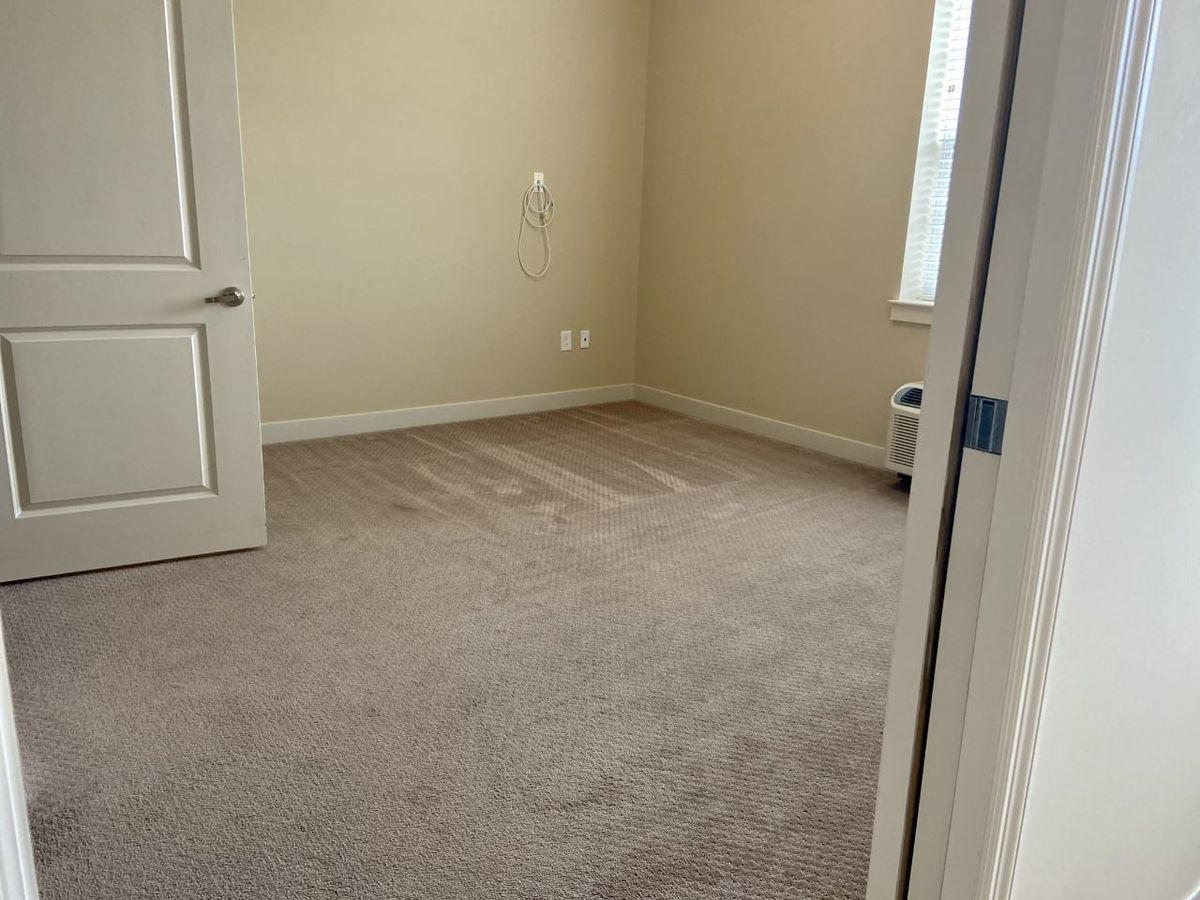 An empty carpeted room with a door and window.